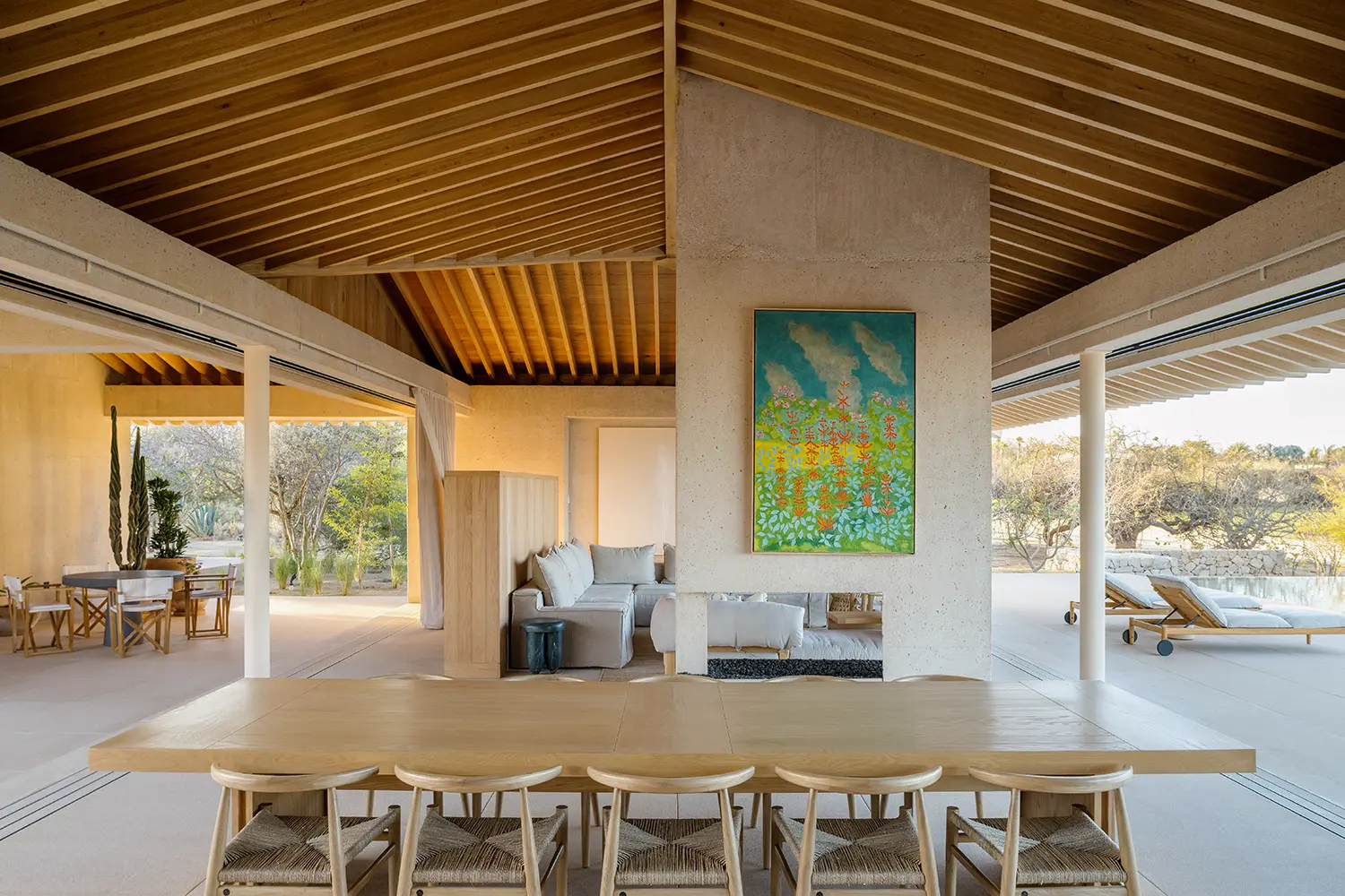 Bright open-plan living and dining space with a colorful abstract painting on a concrete wall and views of the pool.