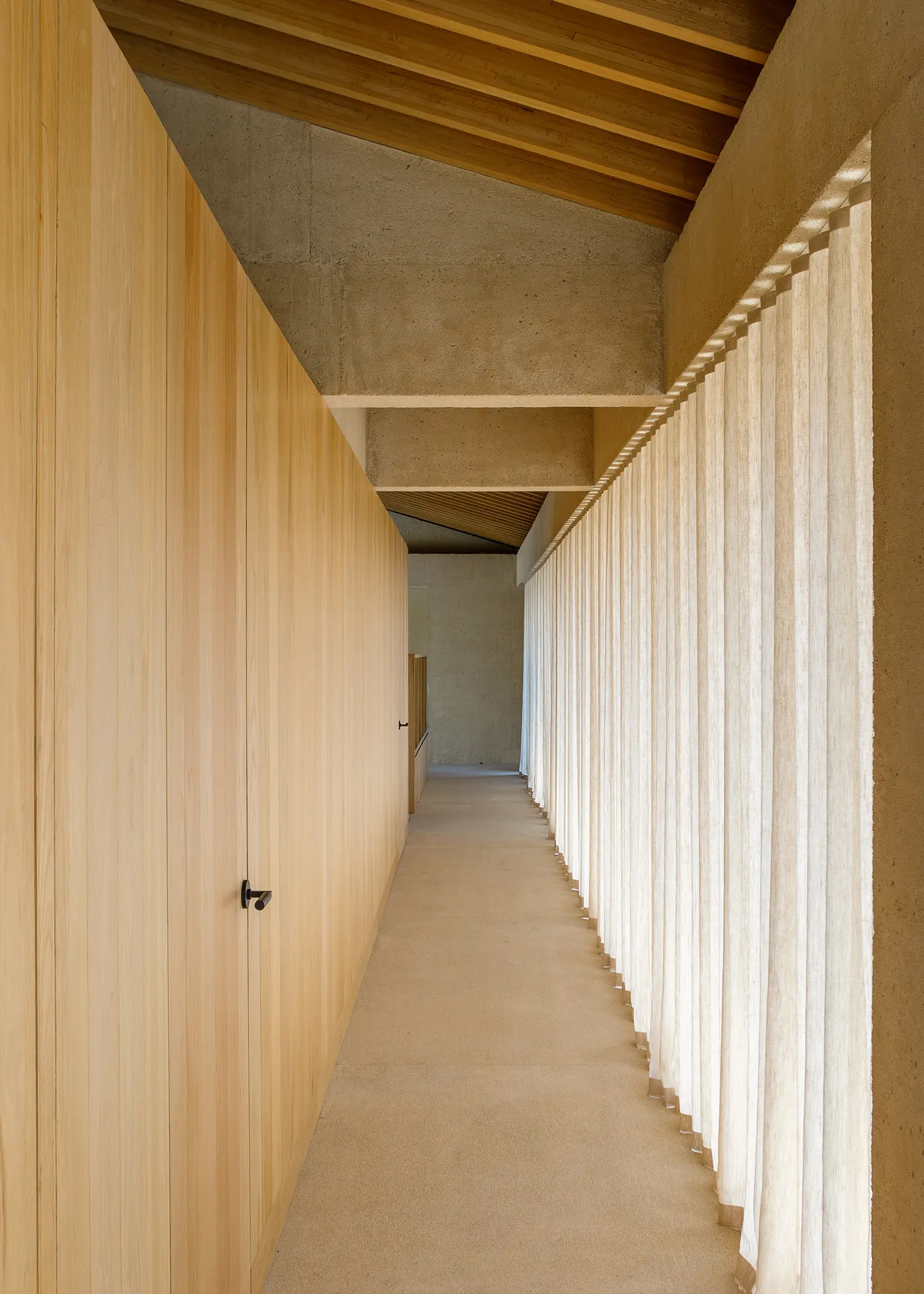 Minimalist corridor with light wood paneling on one side and a long, translucent white curtain on the other.