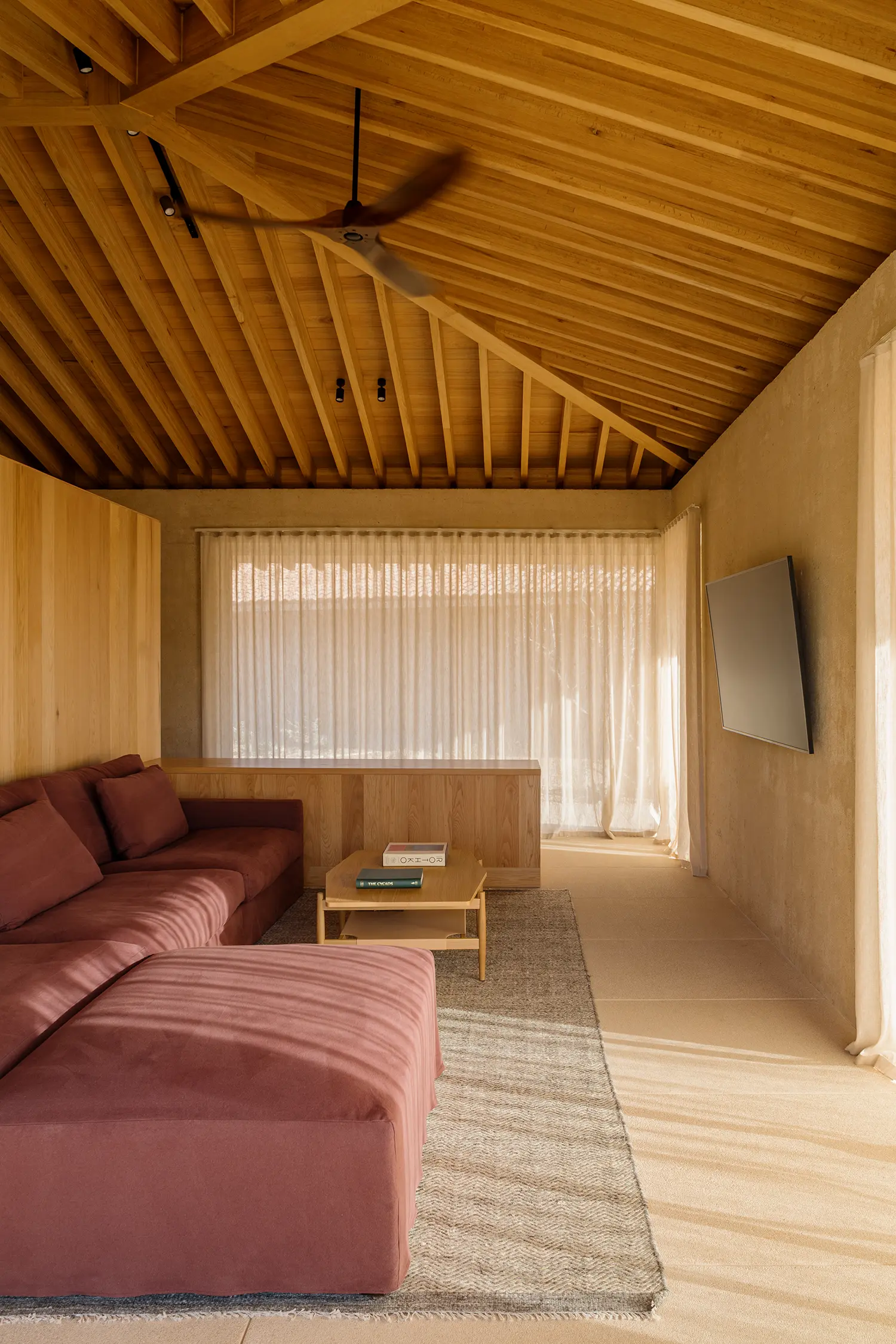 Cozy family room with a mauve-colored sectional sofa and a wooden ceiling fan under the pitched oak roof.