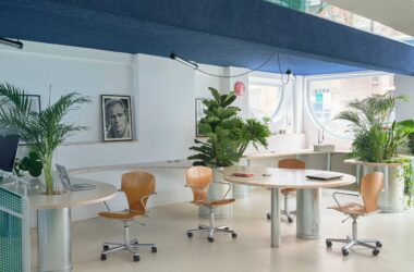 Curving wooden continuous table with integrated plants and Marlon Brando portrait in Madrid office.