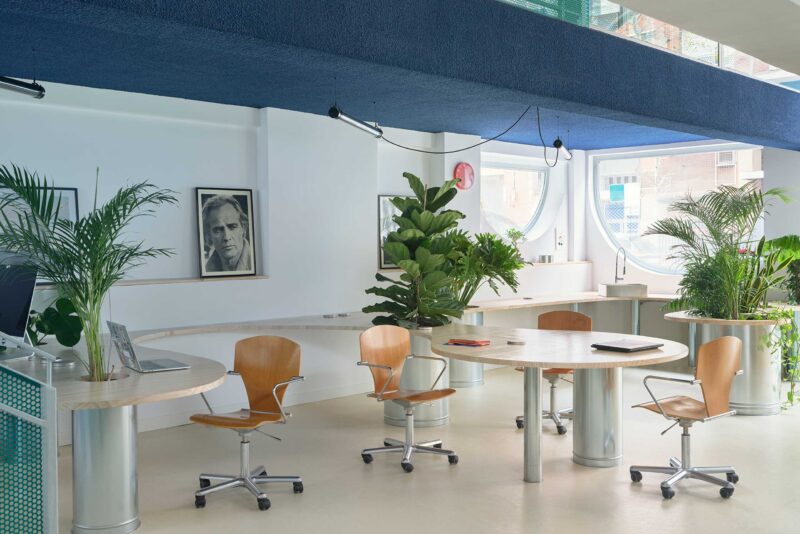 Curving wooden continuous table with integrated plants and Marlon Brando portrait in Madrid office.