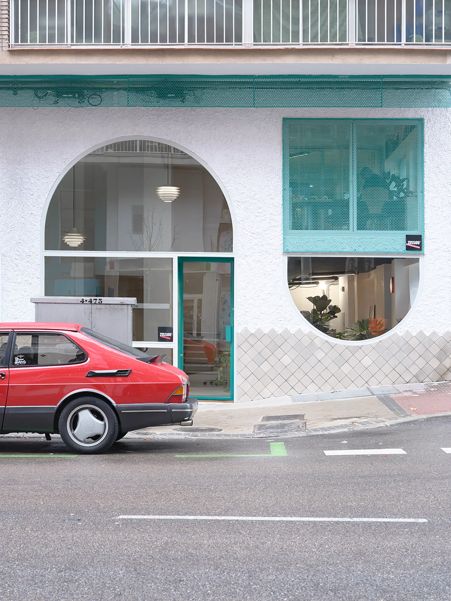 Exterior facade of ZISSOU office in Madrid with arched windows and a vintage red Saab parked outside.