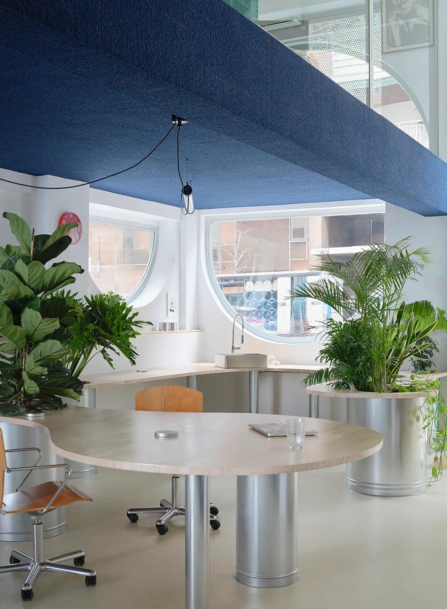 Integrated office kitchen and meeting area with a continuous wooden table and circular windows.