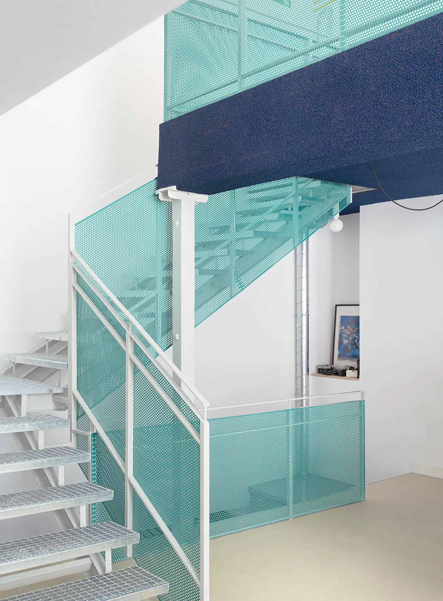 Industrial staircase with teal perforated metal railings and galvanized steel grating treads.