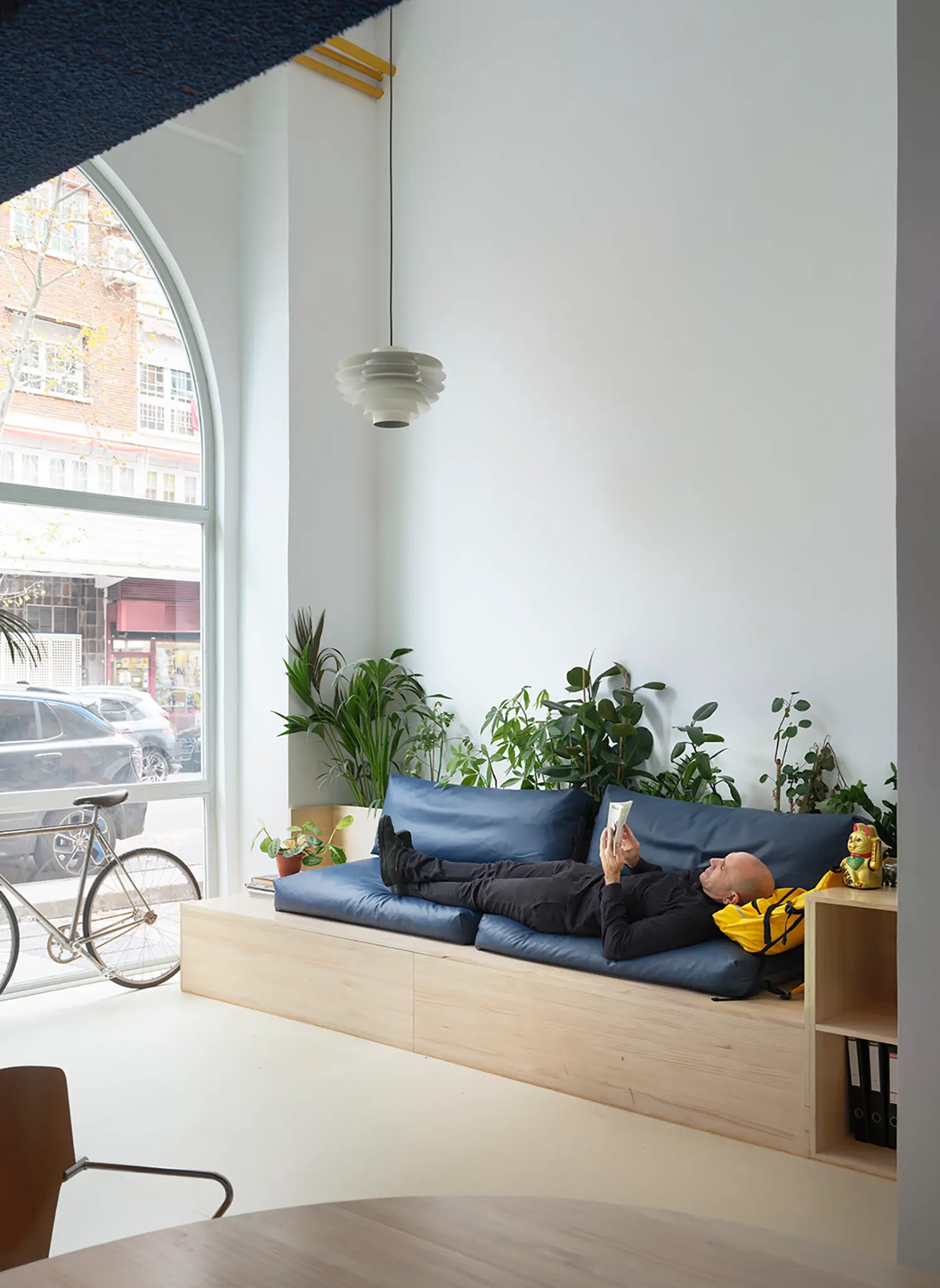 Person reading on a blue built-in sofa next to a large arched window in a Madrid office.