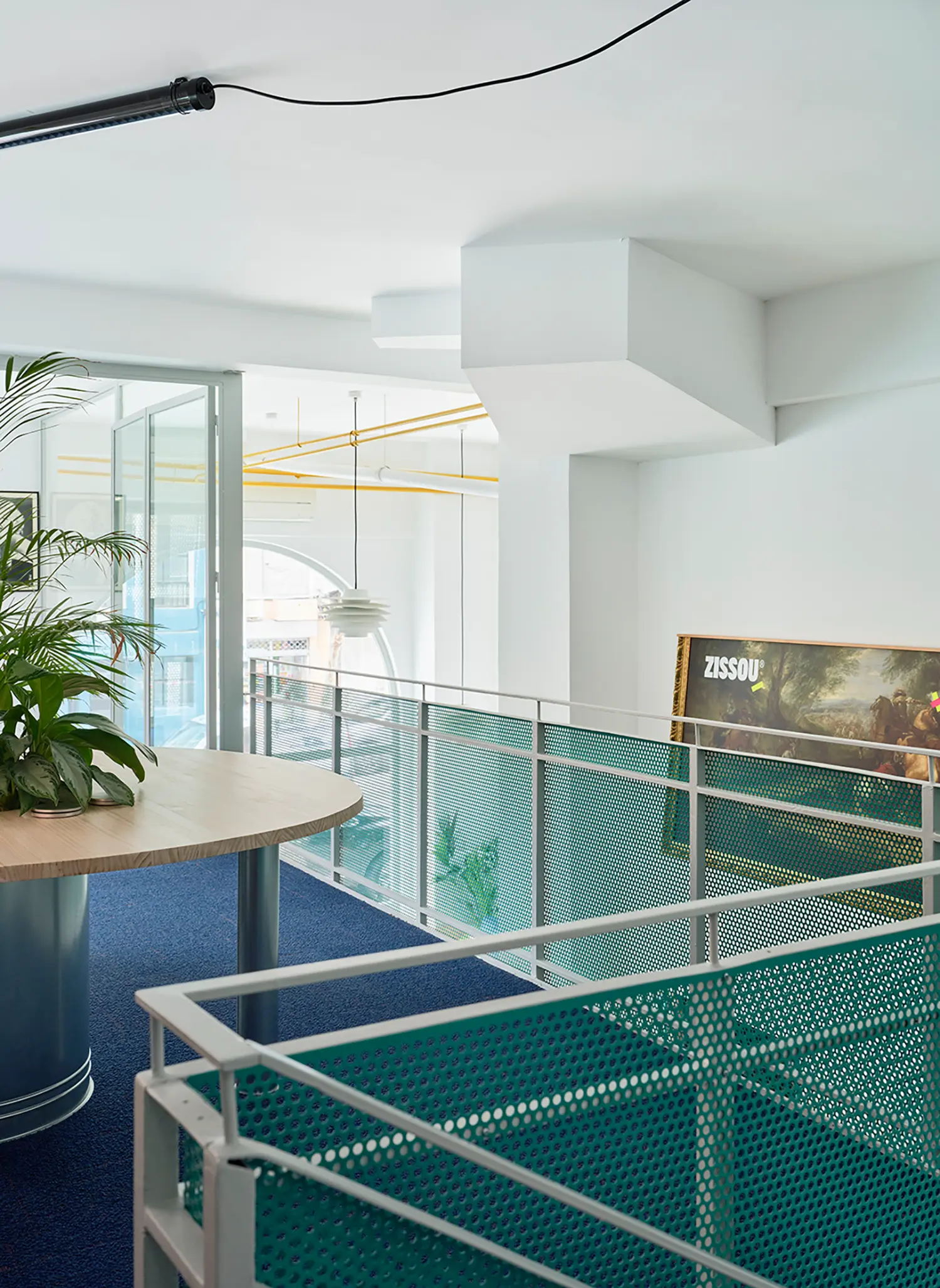 Mezzanine level view with blue carpet, teal metal mesh railings, and a "ZISSOU" branded artwork.