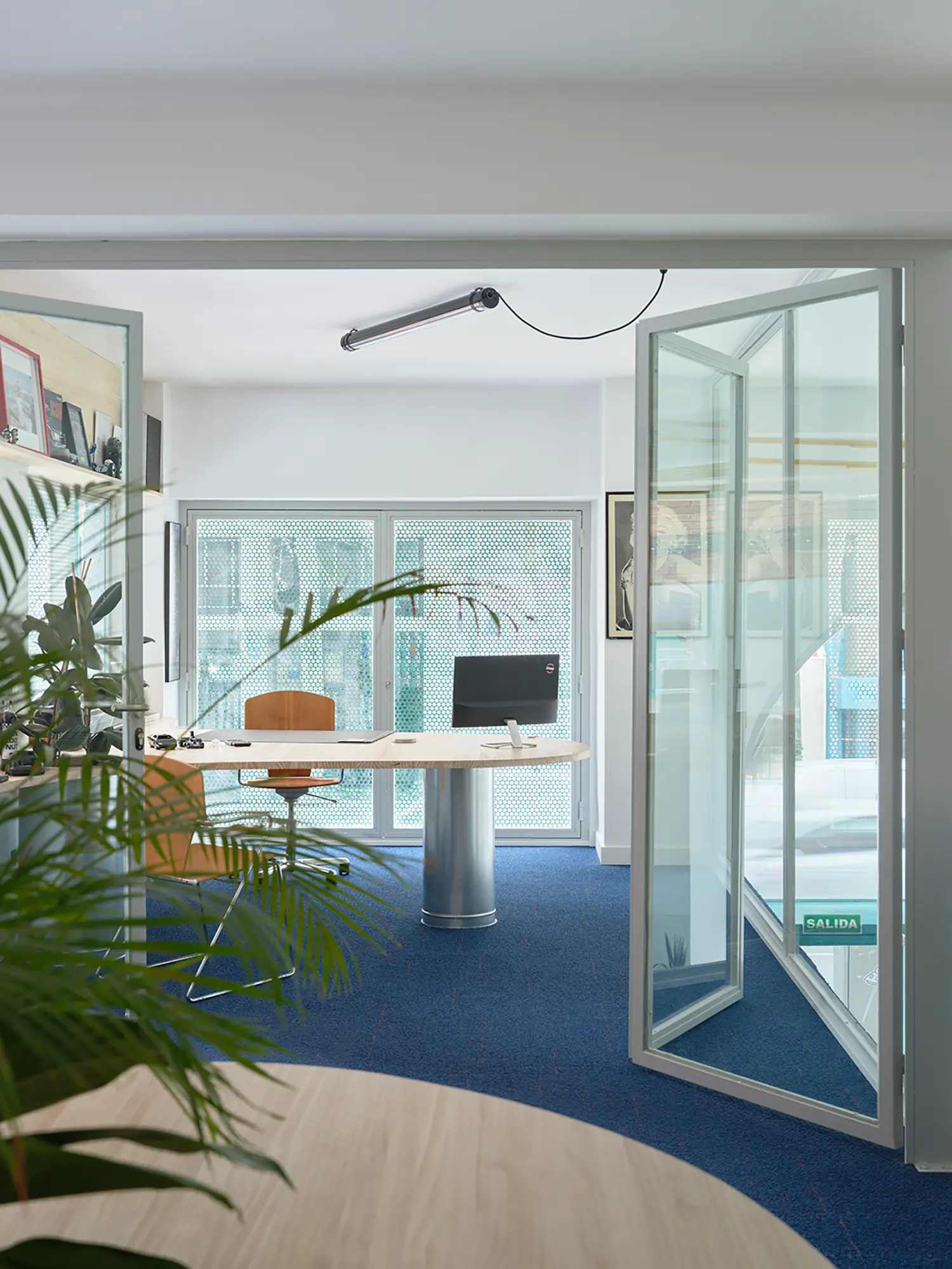 Private office on the mezzanine with glass doors, blue carpet, and perforated metal window screens.