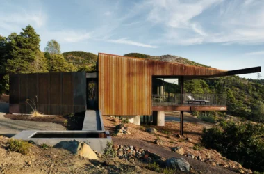 A cantilevered Corten steel house with a concrete entry ramp and water basin in California.