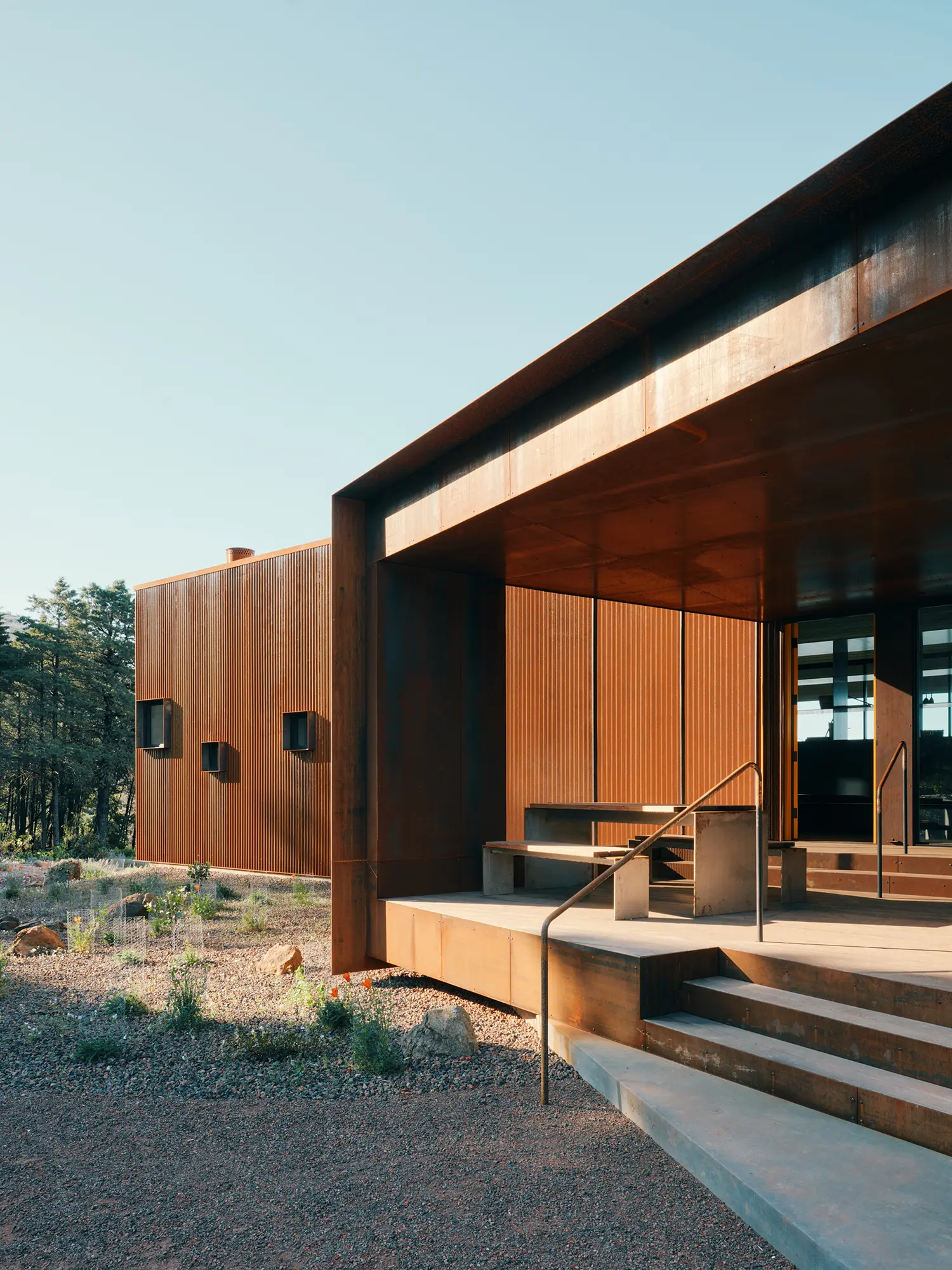 Exterior detail of weathered steel cladding and a concrete porch with integrated seating.