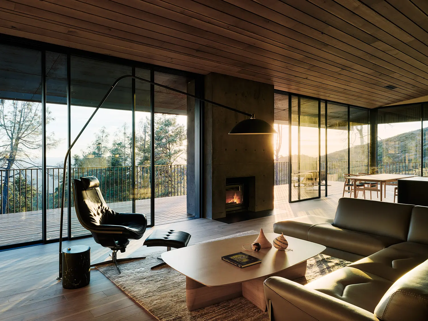 Living room with a concrete fireplace, modern furniture, and large windows at sunset.