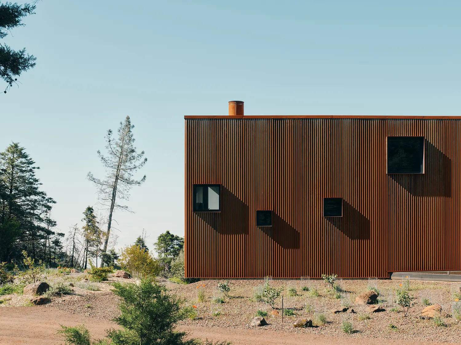 Side profile of a corrugated metal building with small square windows against a clear sky.