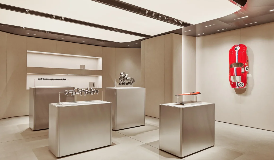 Automotive engine components displayed on minimalist silver plinths in a neutral gallery setting.