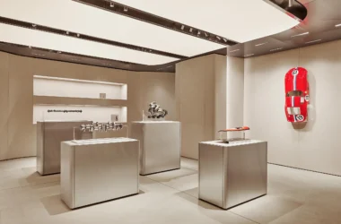 Automotive engine components displayed on minimalist silver plinths in a neutral gallery setting.