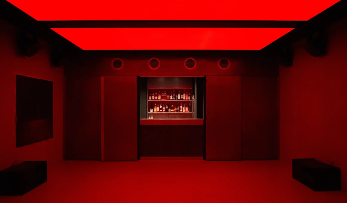 Underground club interior at FEAT. Milan featuring a vibrant red RGB luminous ceiling and a minimalist bar counter.