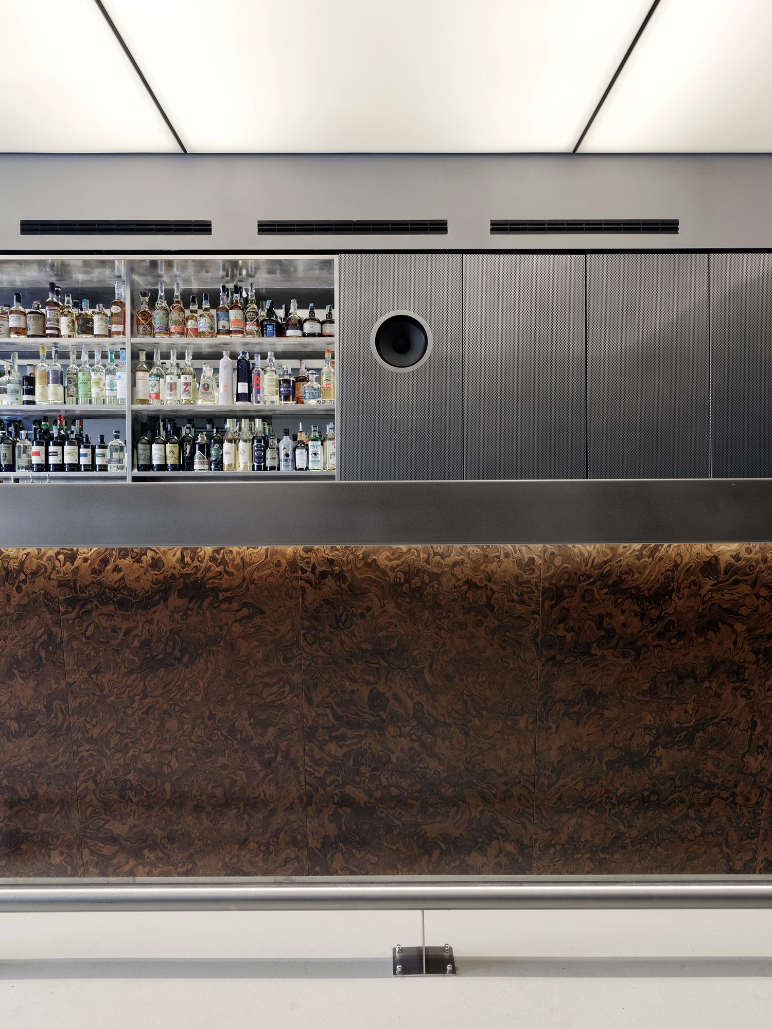 Detailed view of the eight-meter bar counter at FEAT. featuring burl wood panels and a perforated steel back wall.