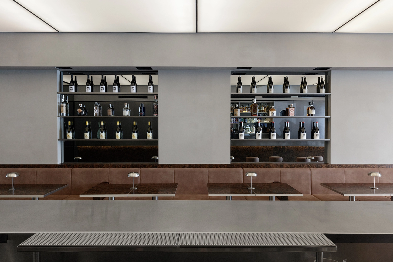 Linear seating area at FEAT. Milan with tan leather benches, burl wood tables, and integrated bottle shelving.