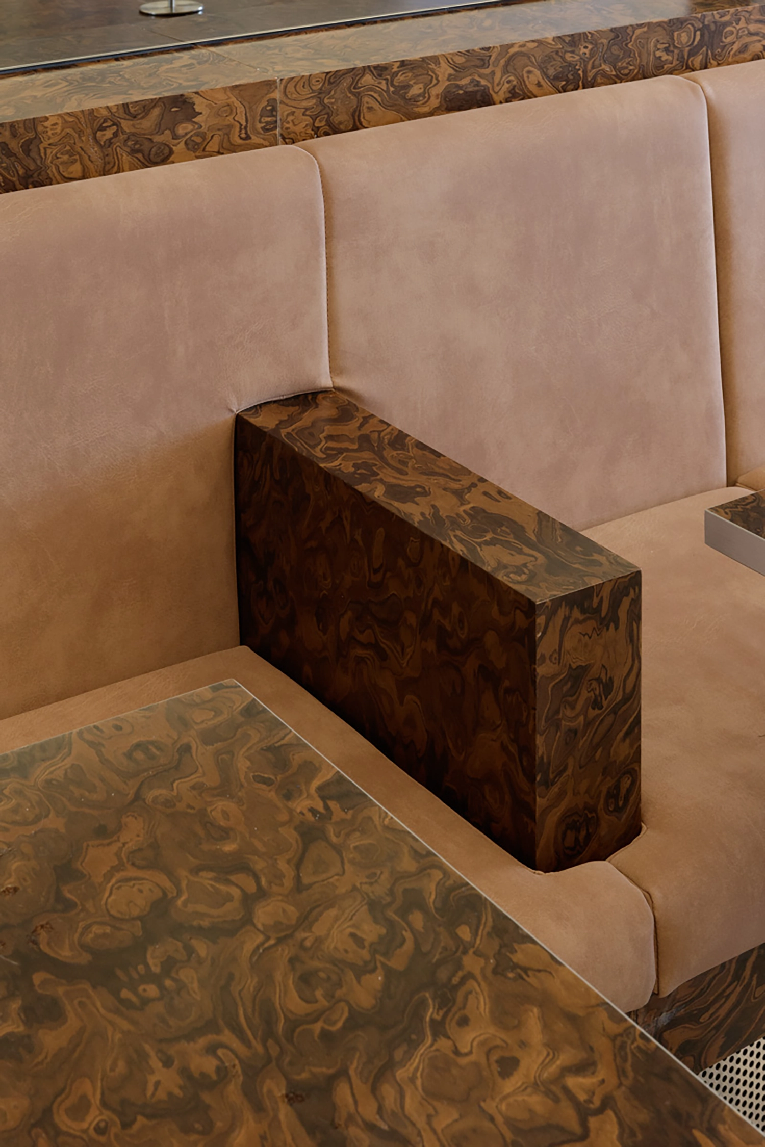 Vertical detail of a tan leather bench with a blocky burl wood armrest and matching table top.