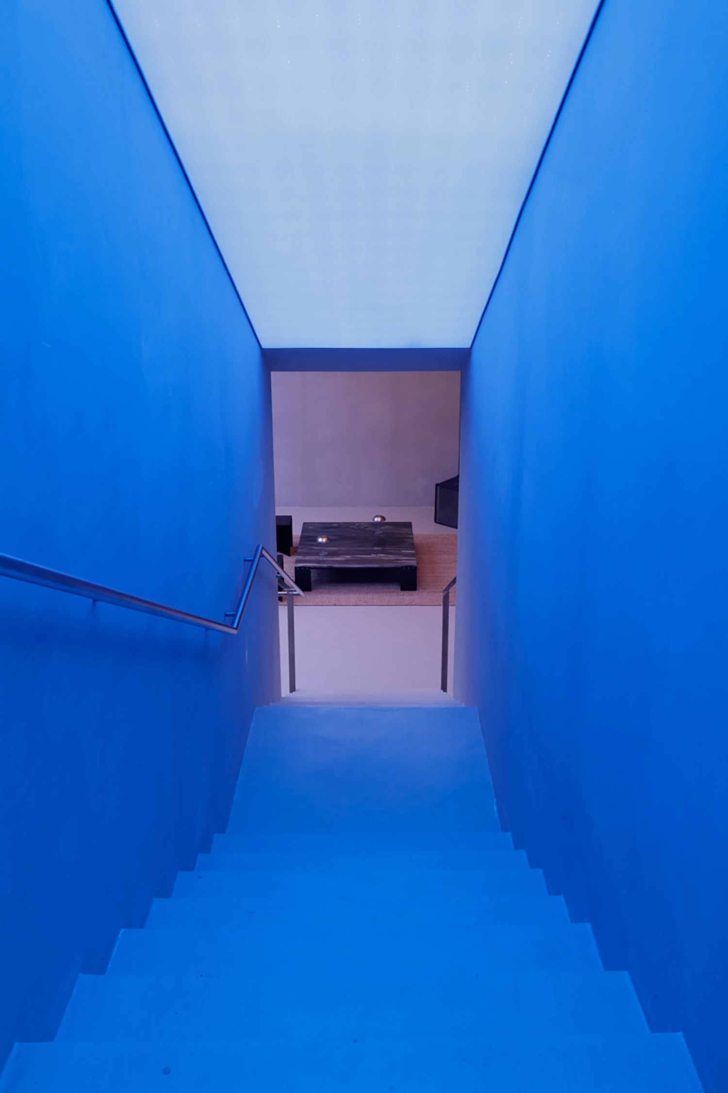 Minimalist staircase at FEAT. descending into a blue-lit subterranean chamber.