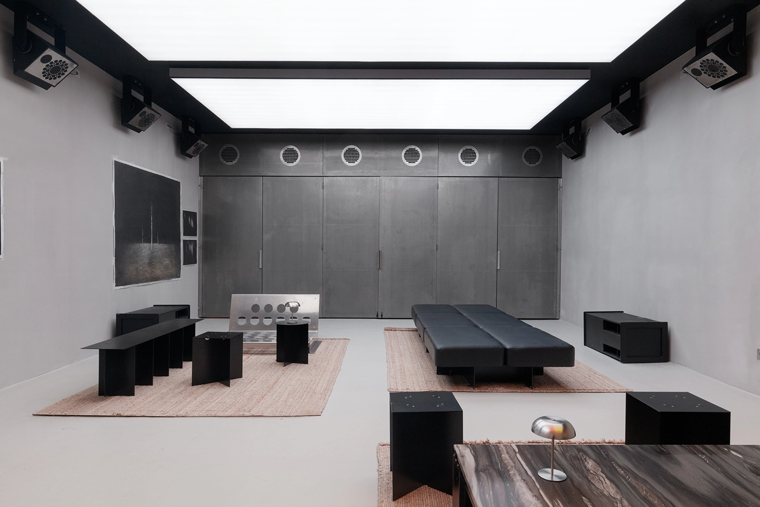 Flexible club chamber at FEAT. with grey industrial walls, luminous ceiling panels, and minimalist black furniture.