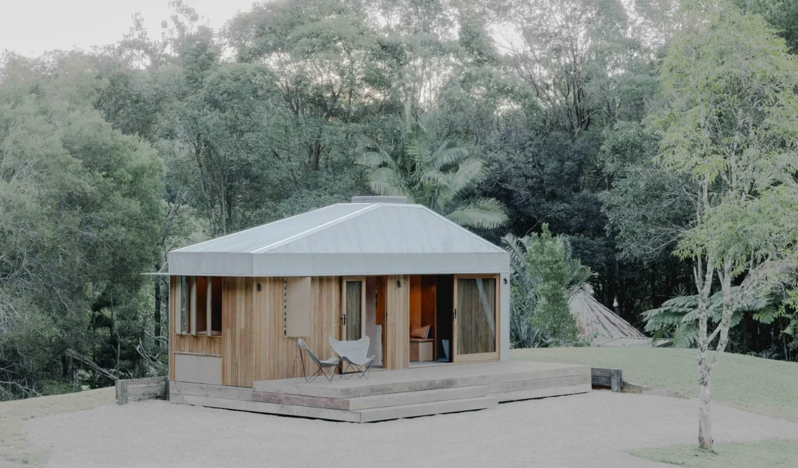 Exterior view of Oculus by Hayley Pryor Architect, a timber-clad tiny house with a silver metal roof set on a gravel clearing in Byron Bay.