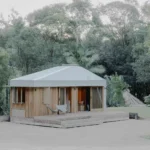 Exterior view of Oculus by Hayley Pryor Architect, a timber-clad tiny house with a silver metal roof set on a gravel clearing in Byron Bay.
