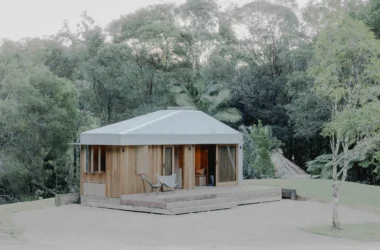 Exterior view of Oculus by Hayley Pryor Architect, a timber-clad tiny house with a silver metal roof set on a gravel clearing in Byron Bay.
