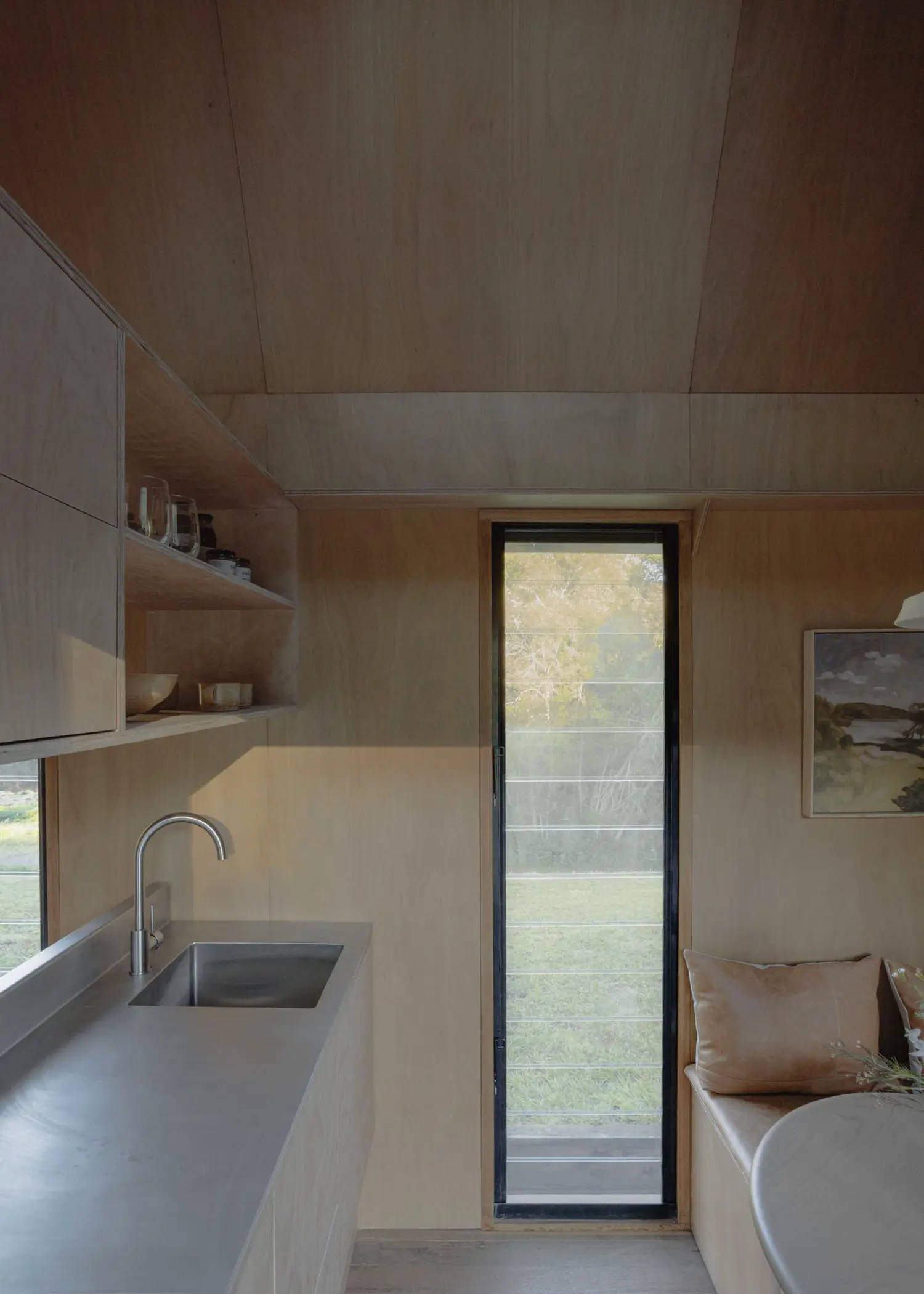 View of the minimalist stainless steel kitchenette in Oculus, positioned next to a tall, narrow louvered window.