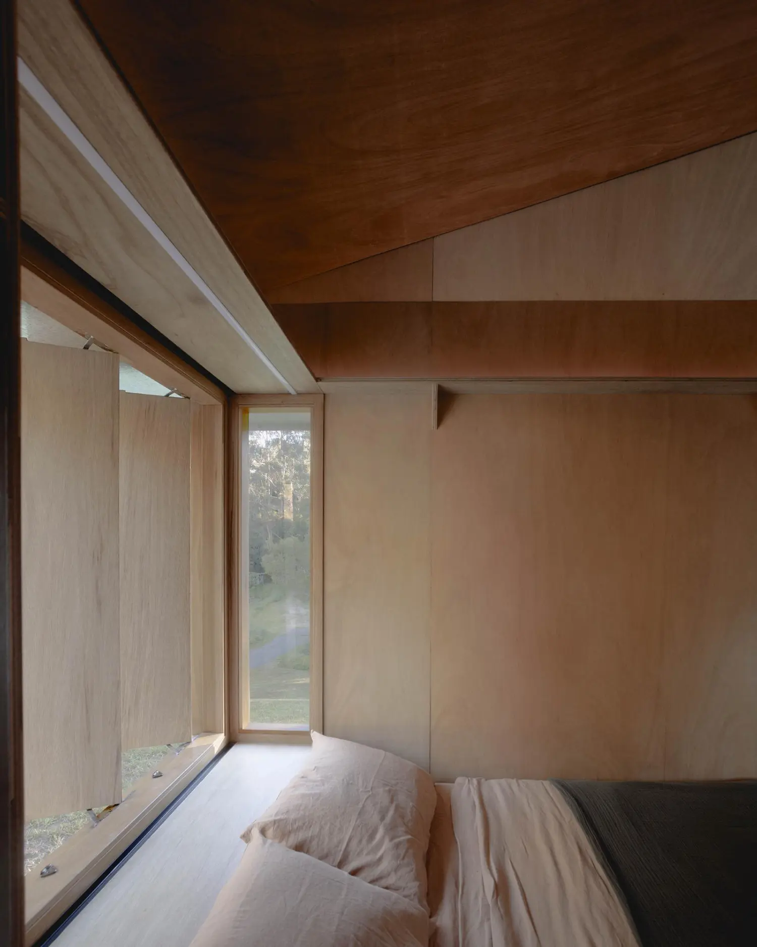 Interior of the sleeping platform in Oculus, featuring a bed tucked against a window with timber shutters and views of the forest.