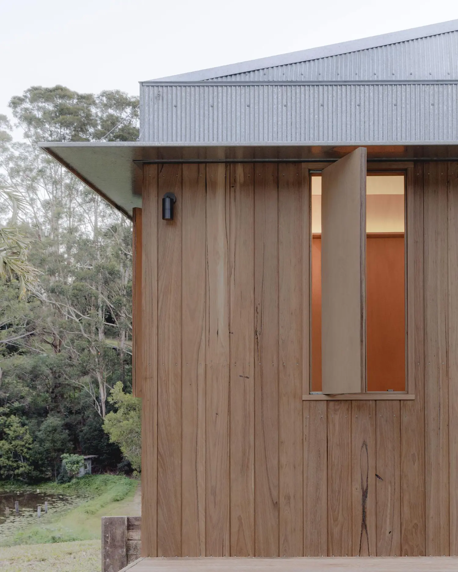 Close-up of the exterior timber corner of Oculus, showing a minimalist black outdoor light and a timber window shutter.