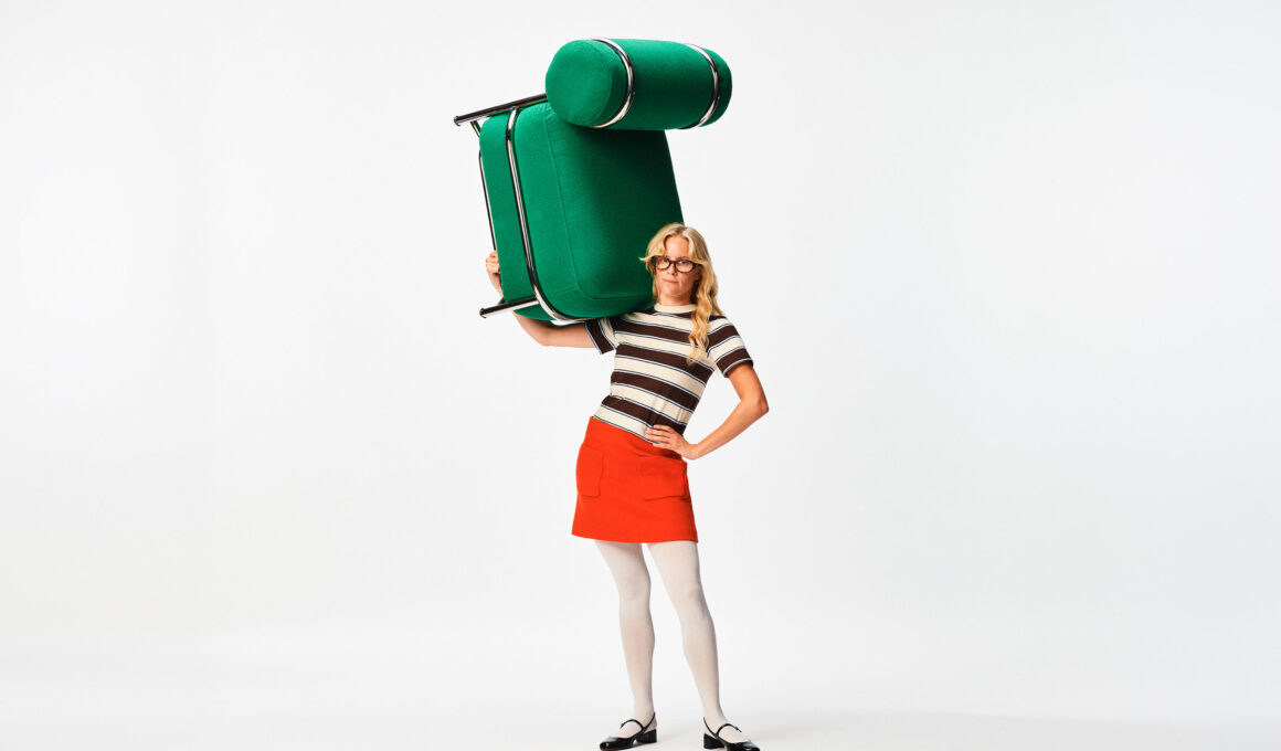 A person carrying a large emerald green IKEA PS 2026 inflatable easy chair on their shoulder against a white background.