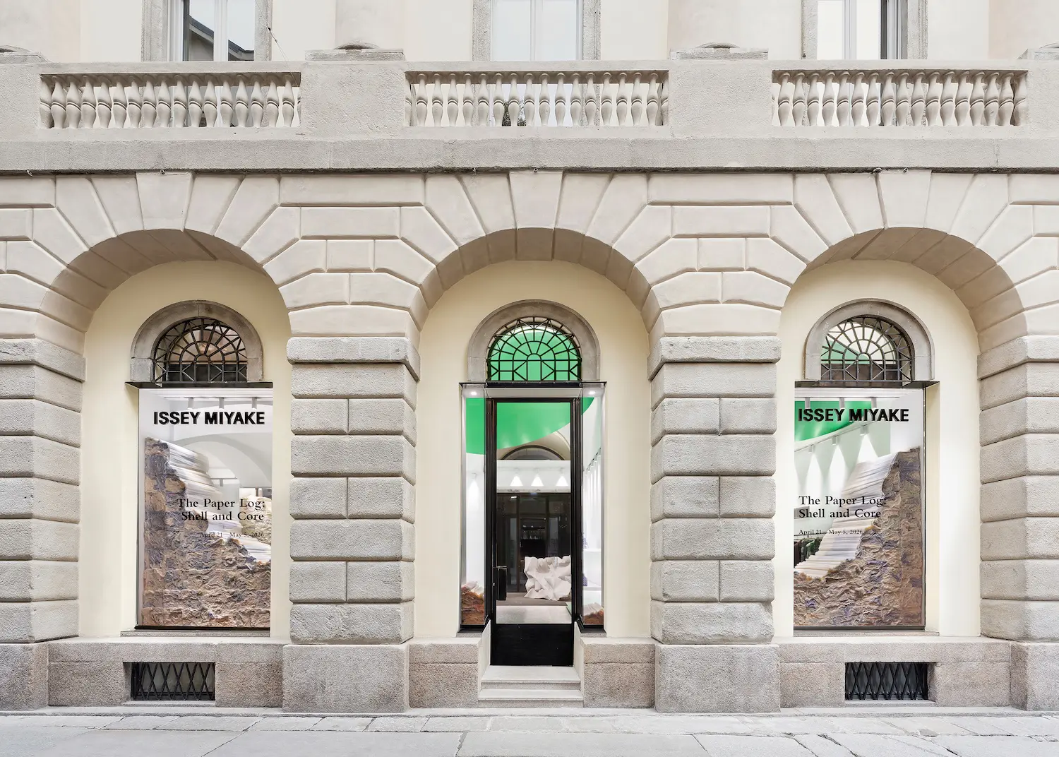 Exterior stone facade of the ISSEY MIYAKE store on Via Bagutta with large arched windows displaying exhibition posters.