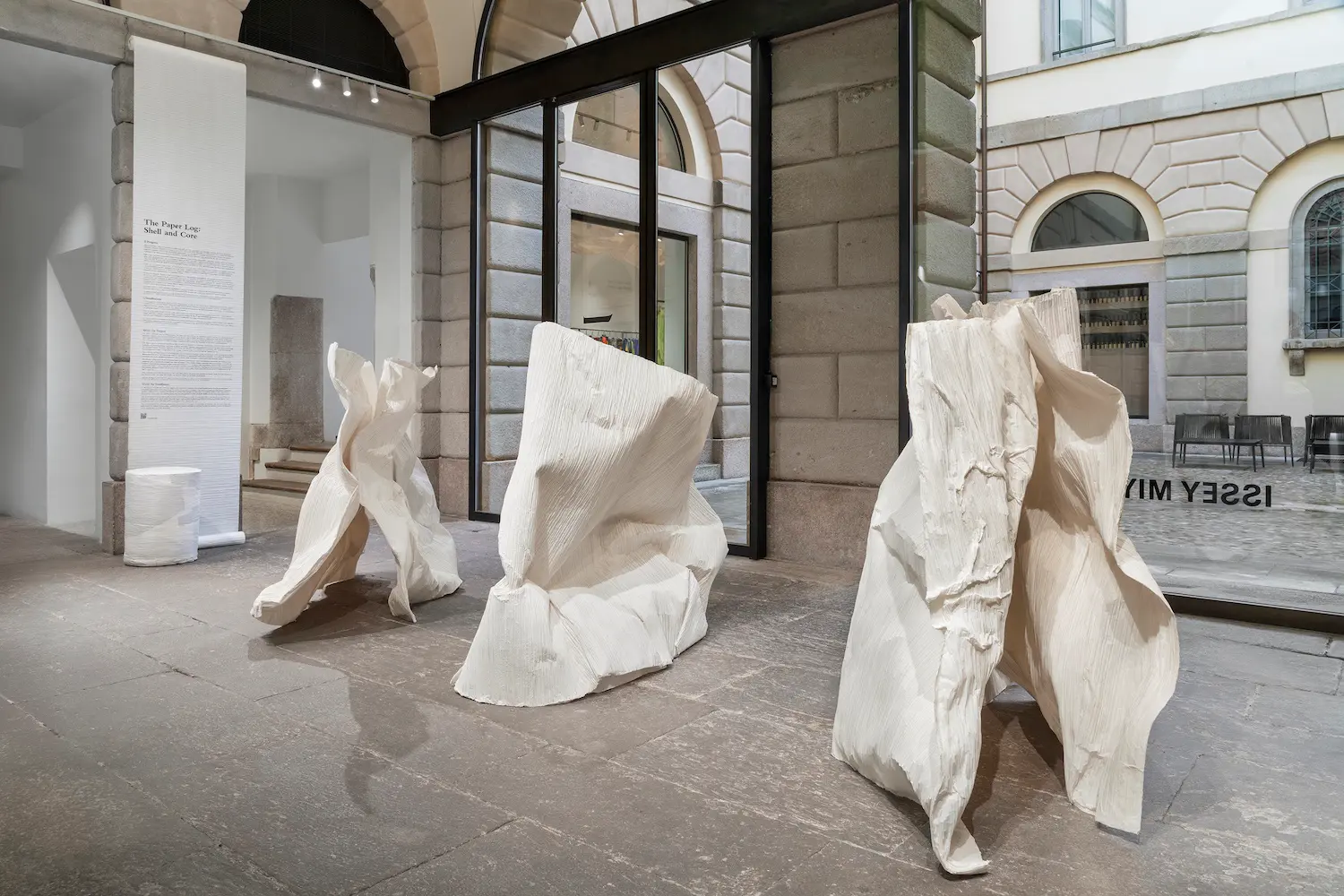Three large, white "Shell" sculptures with petrified pleats standing in a stone-floored courtyard.
