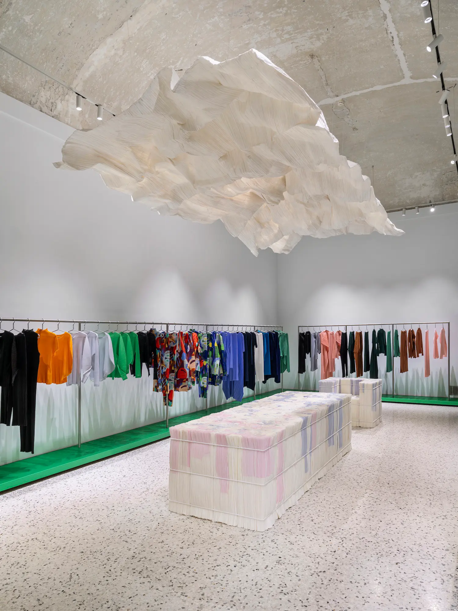 Showroom with colorful garments, a large pleated paper cloud suspended from the ceiling, and a long paper table.