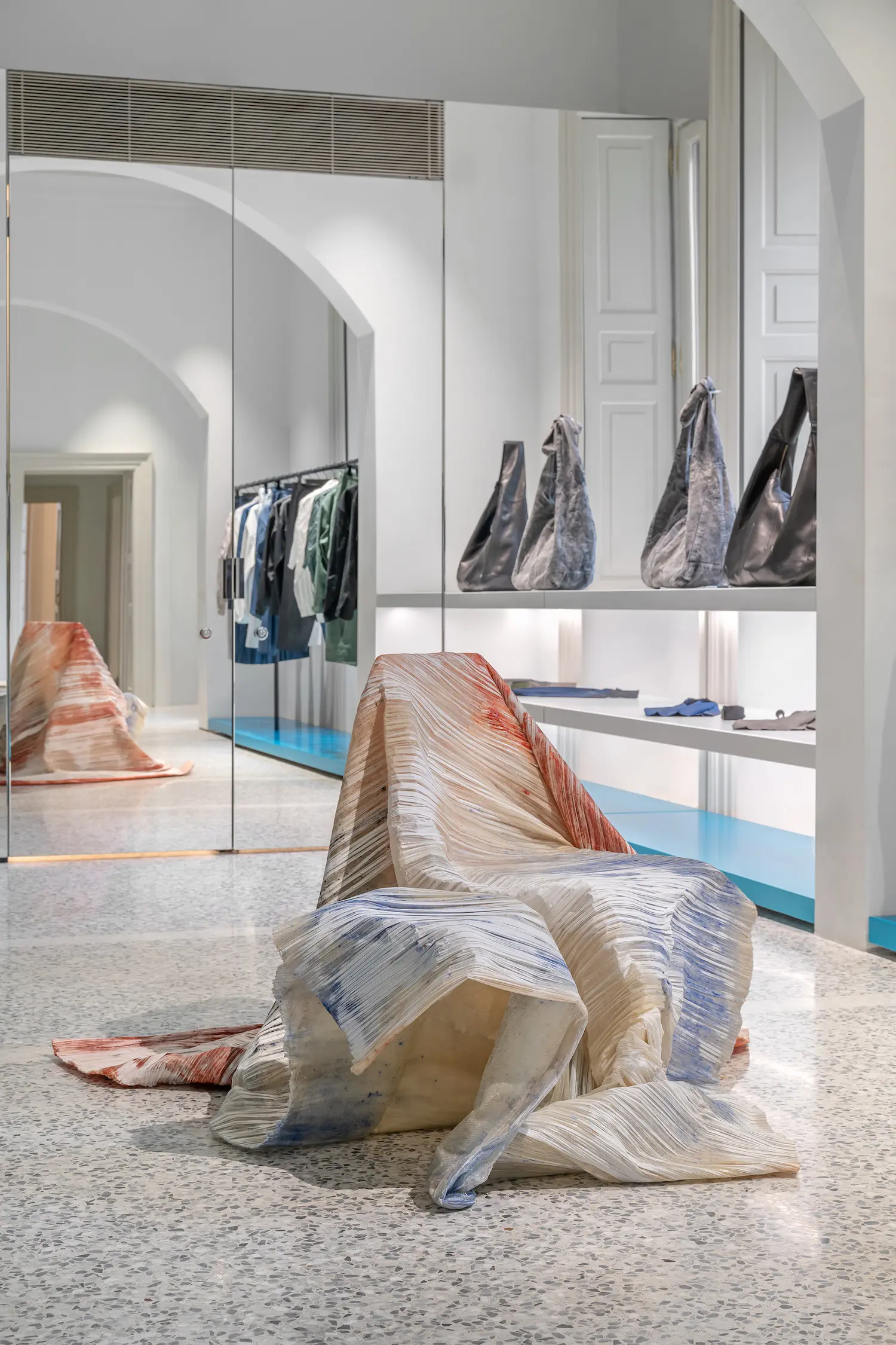 A chair sculpture wrapped in thin, colorful pleated paper standing on a terrazzo floor.