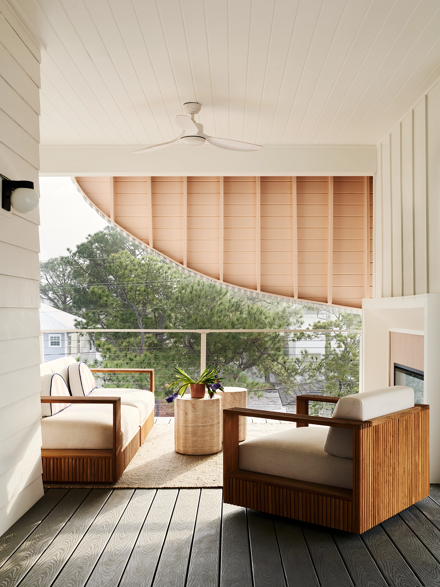 Covered outdoor lounge area with slatted wooden sofas and a curved pink eave overhead.
