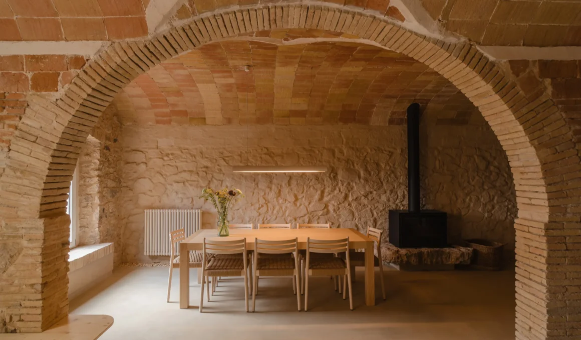 A dining area set under a historic brick Catalan vault with a long wooden table and stone walls.