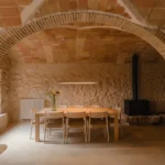A dining area set under a historic brick Catalan vault with a long wooden table and stone walls.