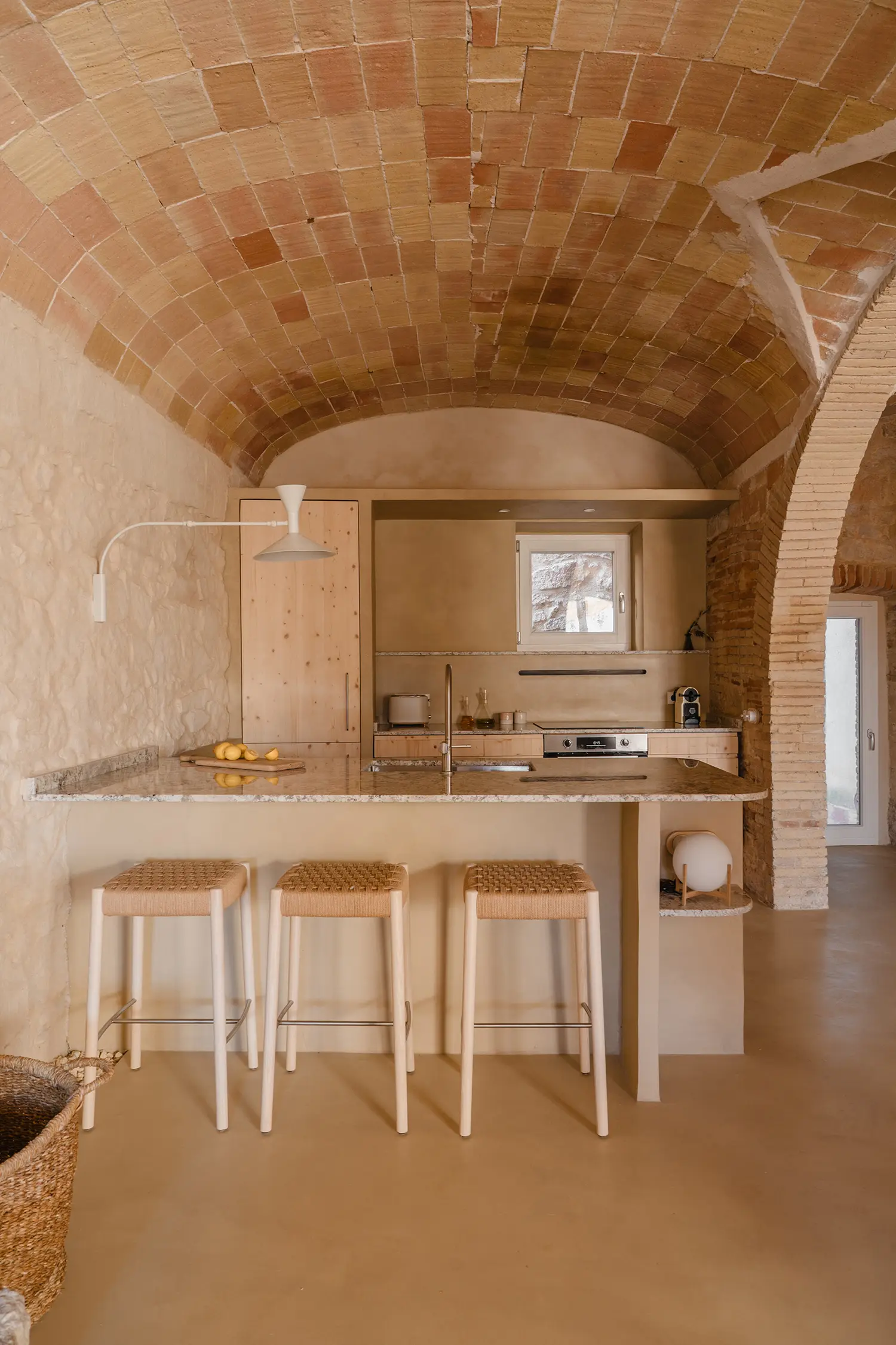 A modern kitchen island with woven bar stools located under a vaulted brick ceiling.