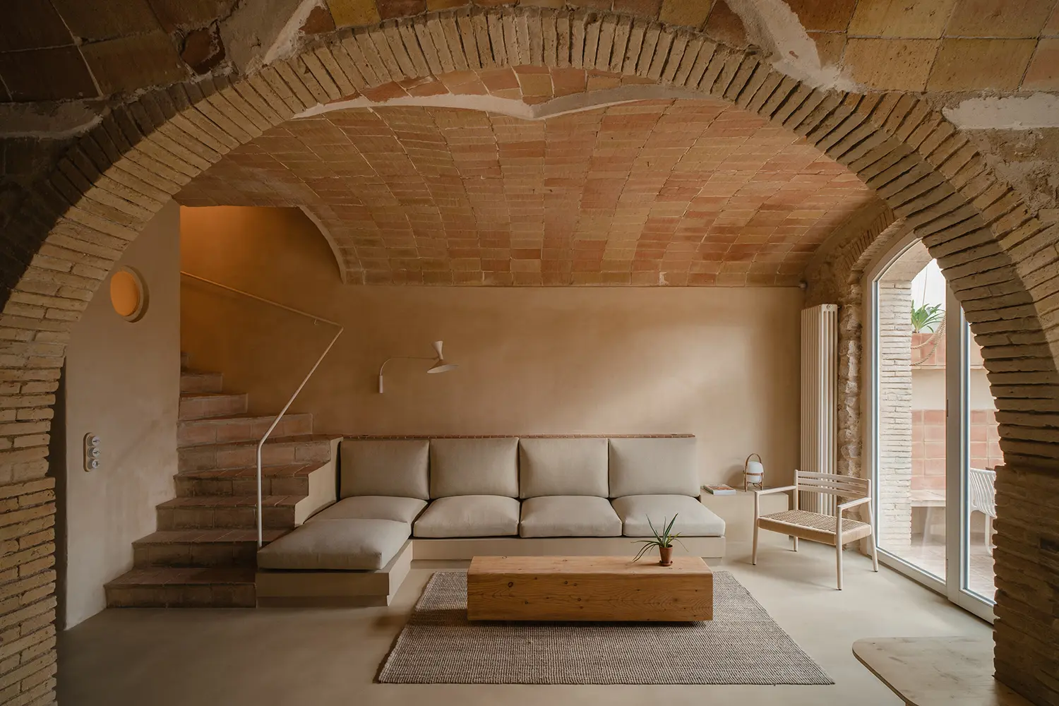 A minimalist living room with a neutral sofa, wooden coffee table, and an exposed brick arch.