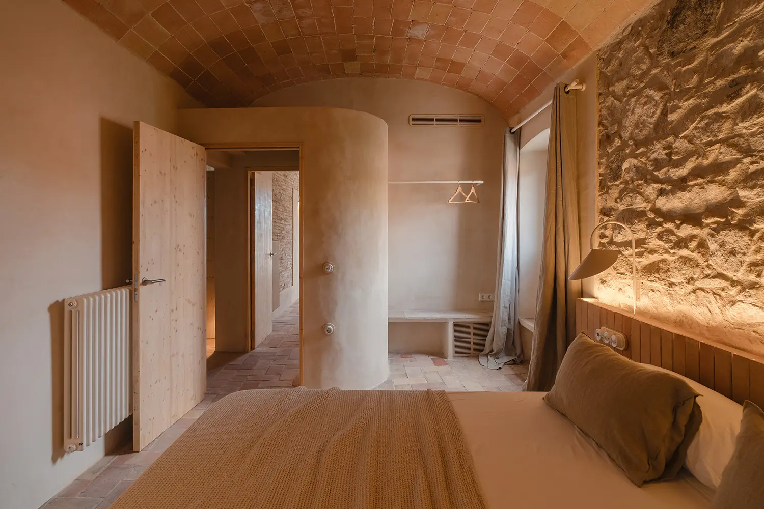 A bedroom with a stone feature wall, vaulted ceiling, and a curved plaster partition.