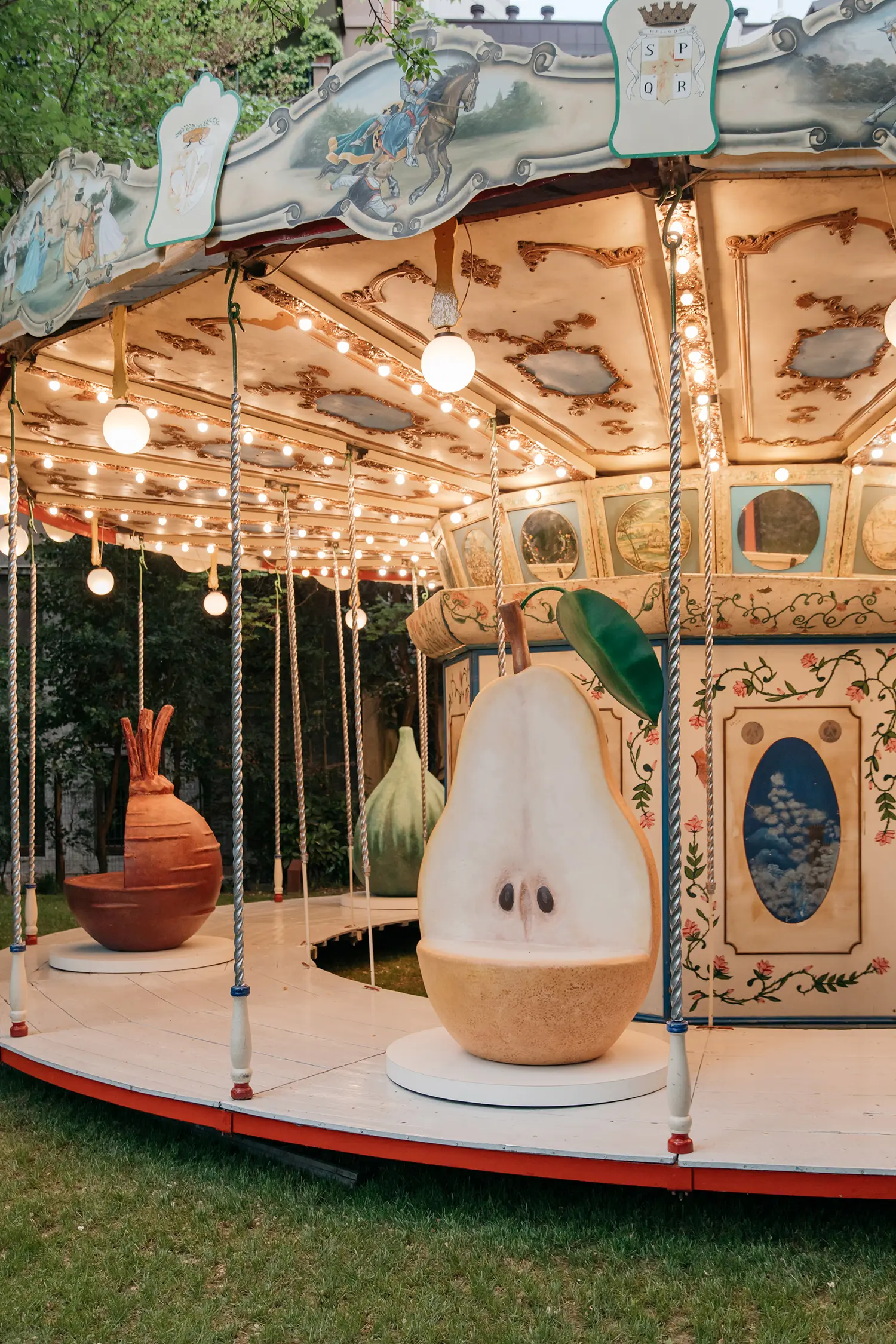 Close-up of a large sculptural pear seat on a vintage carousel with warm fairground lights.