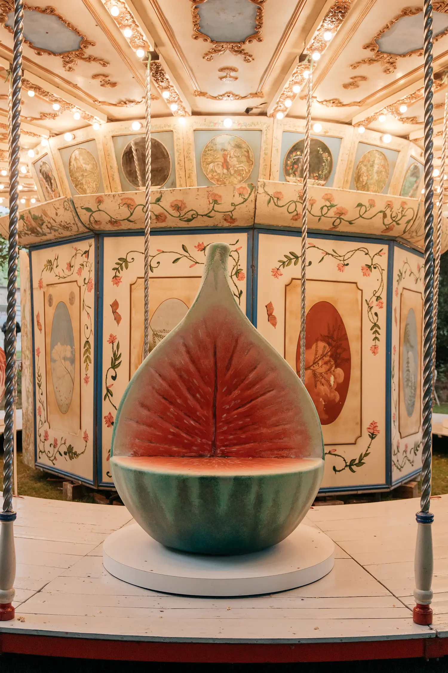 Frontal view of a giant fig sculpture seat with a deep red interior on the carousel platform.