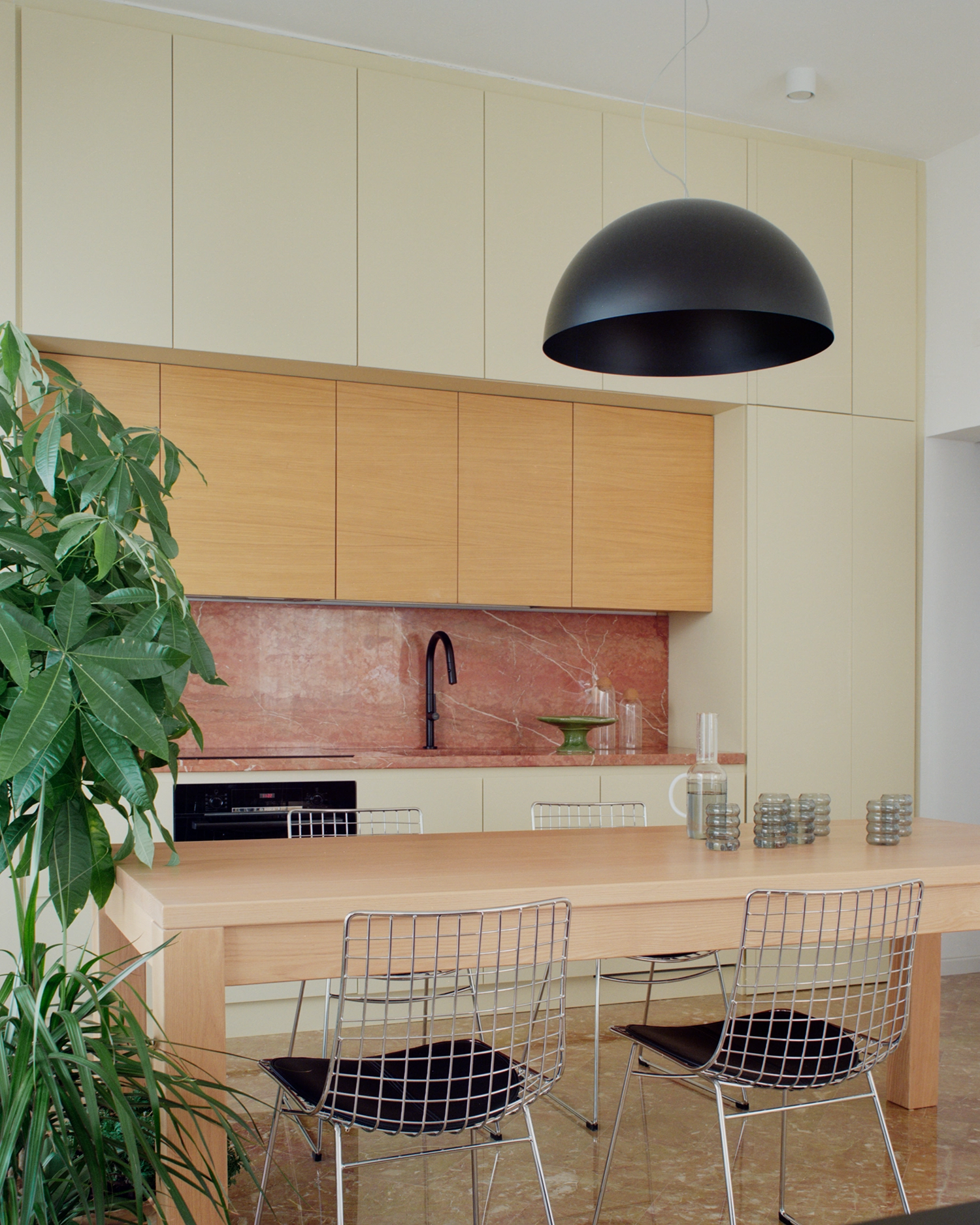 Modern kitchen with Rosa del Garda marble countertops, oak cabinetry, and Bertoia-style wire chairs.