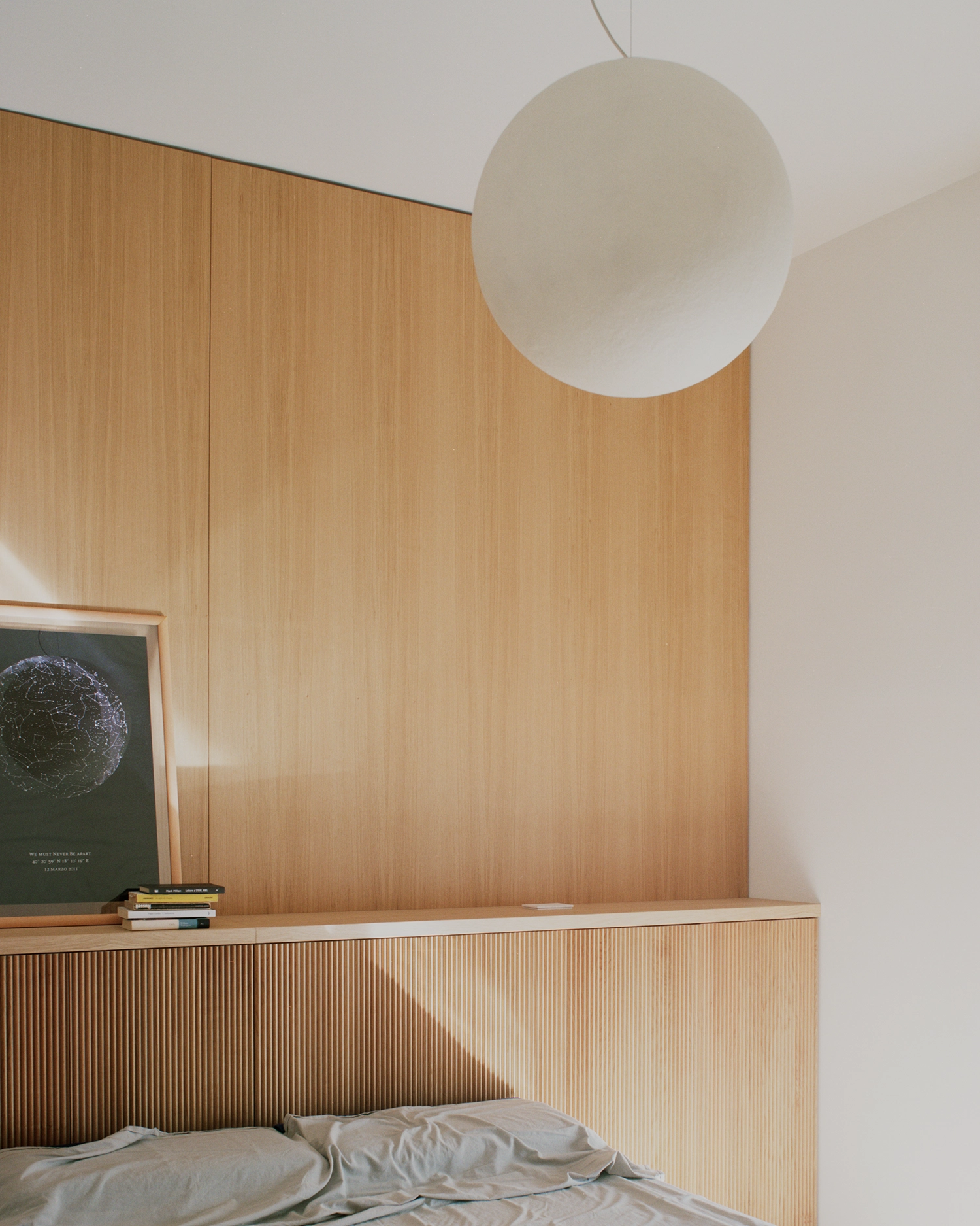 Minimalist bedroom detail with a fluted oak headboard and a spherical white pendant lamp.