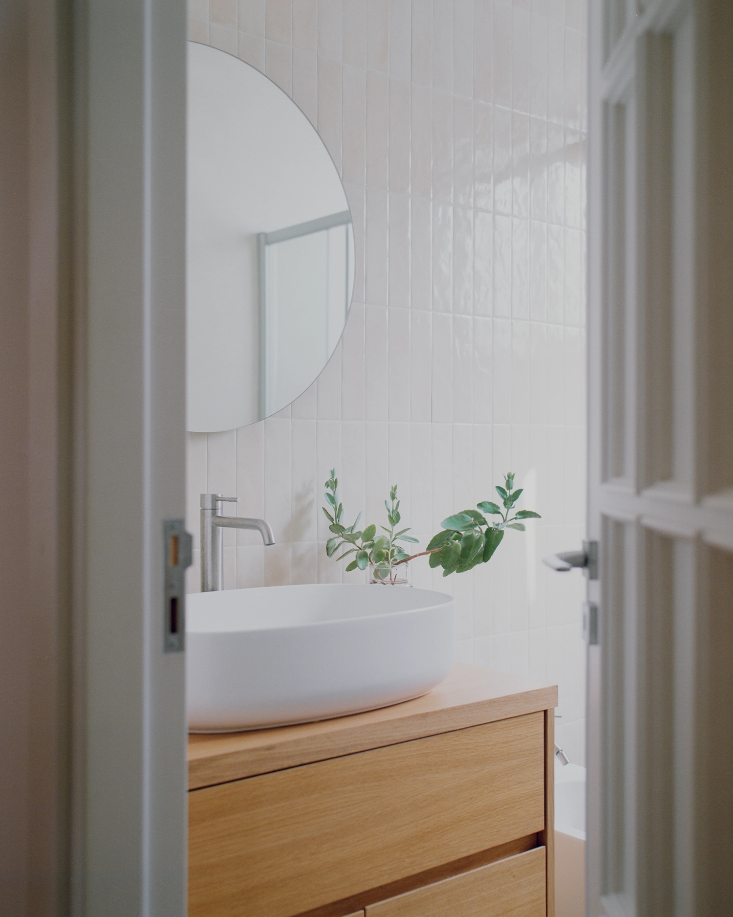 Contemporary bathroom with a white vessel sink, oak vanity, and vertical cream wall tiles.