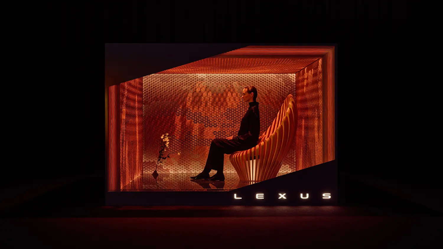 A person sitting on a sculptural wooden chair within a warm, glowing copper-toned architectural frame.