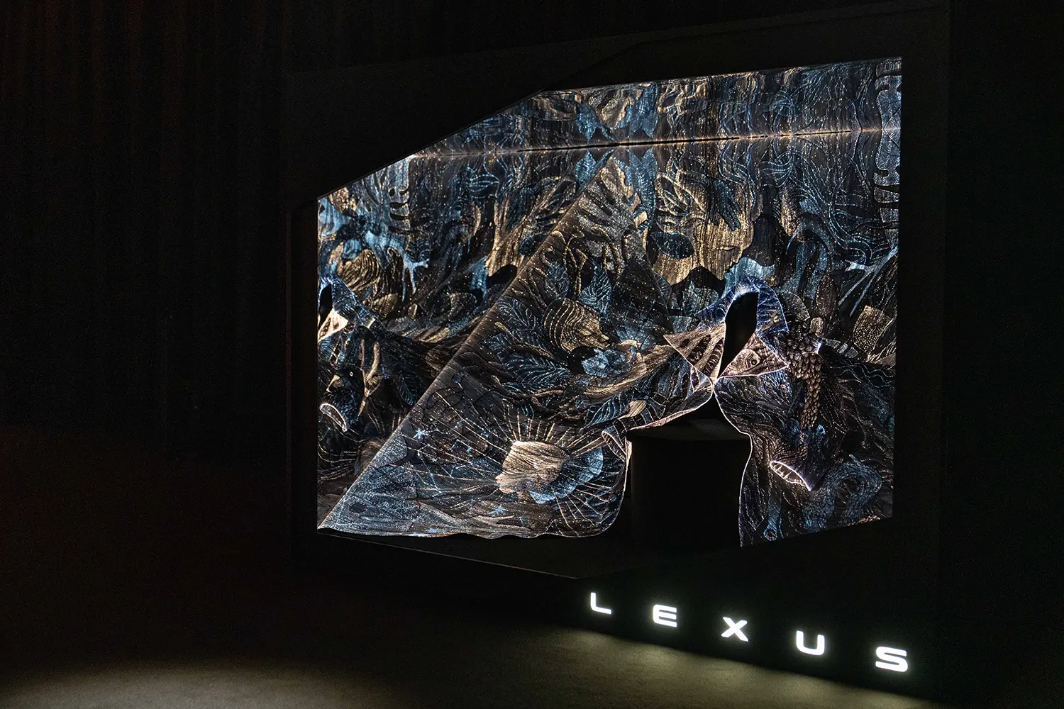 An intricate, glowing textile with fiber-optic embroidery displayed in a dark room.
