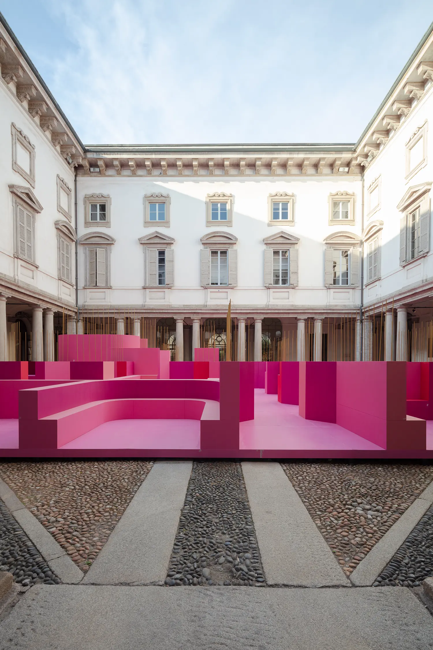 Ground-level wide shot of the pink installation within the courtyard under a soft sky.