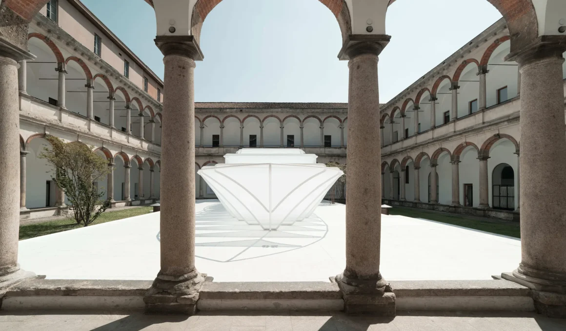 Front view of the UN_Material installation by Piero Lissoni showing the white fabric yacht silhouette framed by the arches of the University of Milan.