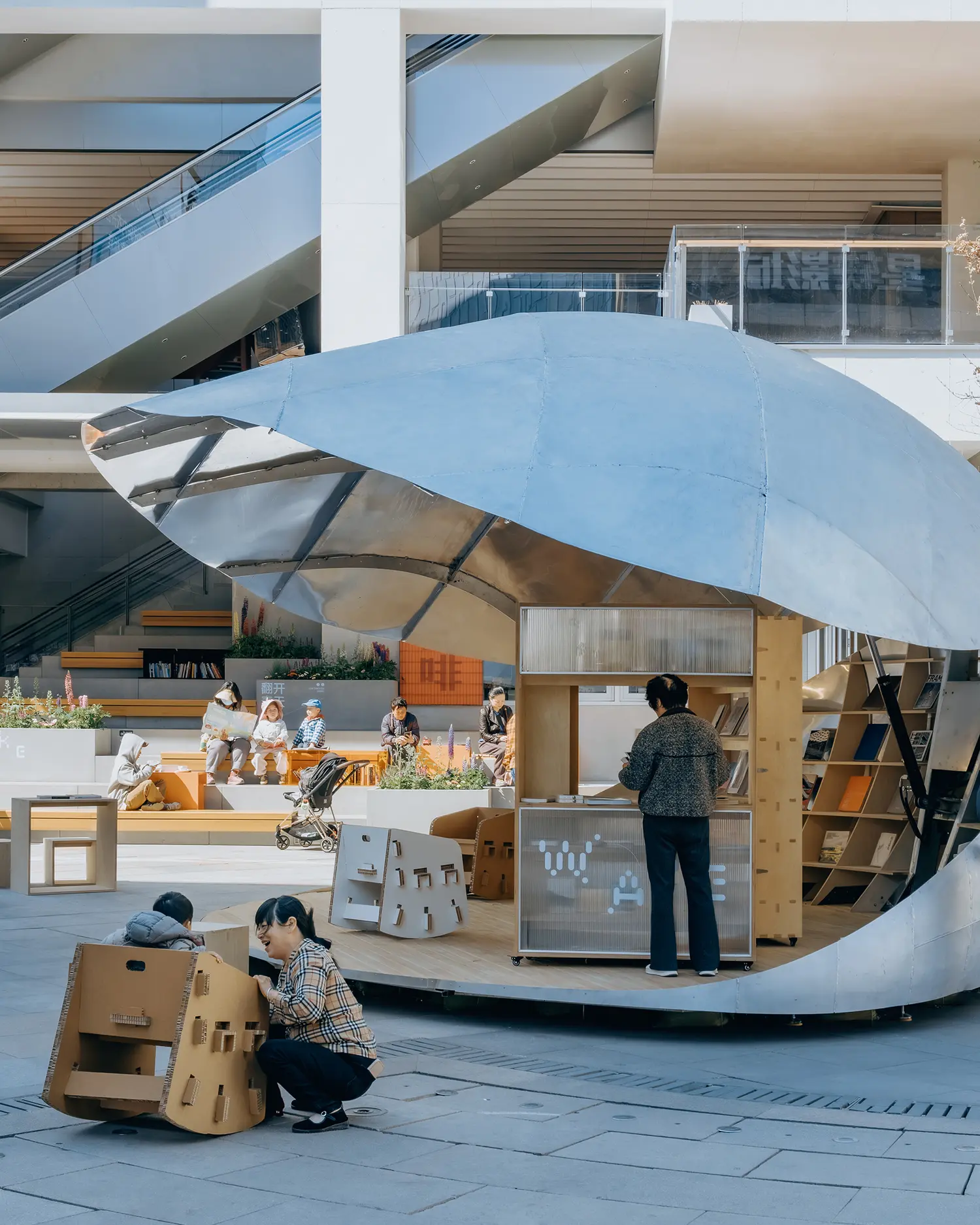 A ground-level view of the metallic pavilion roof partially open, revealing a wooden interior counter and shelving where a person is standing.